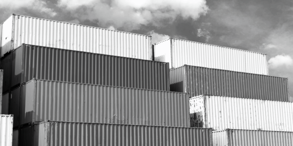 Stacked ISO shipping containers in a port, showing repetition and modular structure under a cloudy sky.